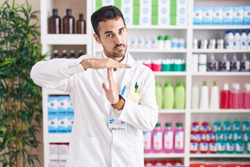 Handsome hispanic man working at pharmacy drugstore doing time out gesture with hands, frustrated...