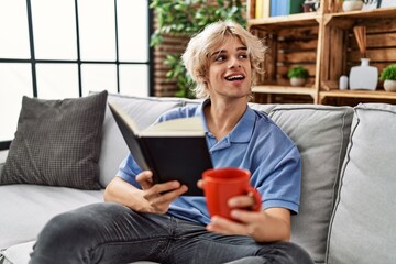 Young blond man reading book and drinking coffee at home