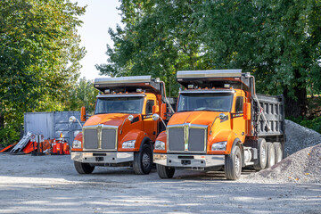 Two orange professional tip trucks standing on the parking lot on the construction side