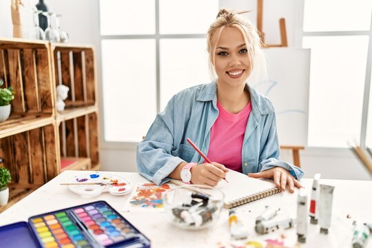 Young caucasian woman artist smiling confident drawing on notebook at art studio