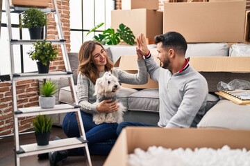 Man and woman high five sitting on floor with dog at new home