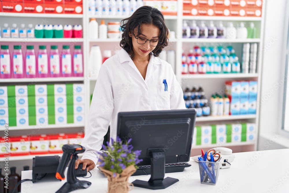 Sticker Young beautiful hispanic woman pharmacist smiling confident using computer at pharmacy