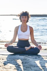 Fototapeta na wymiar Young woman training yoga exercise sitting on sand at seaside
