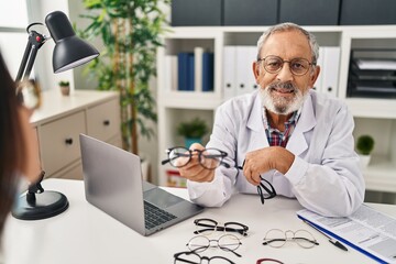 Senior grey-haired man optician holding glasses showing to patient at clinic