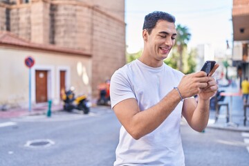 Young hispanic man smiling confident using smartphone at street