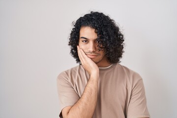 Fototapeta na wymiar Hispanic man with curly hair standing over white background thinking looking tired and bored with depression problems with crossed arms.