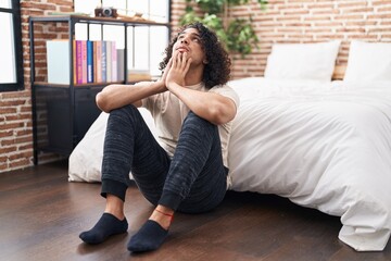 Young latin man stressed sitting on floor at bedroom