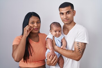 Young hispanic couple with baby standing together over isolated background mouth and lips shut as...