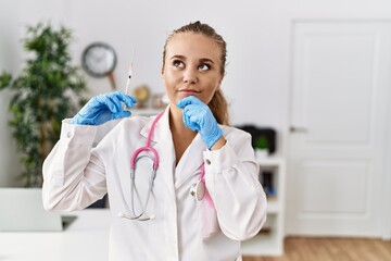 Naklejka premium Young doctor woman holding syringe at the clinic serious face thinking about question with hand on chin, thoughtful about confusing idea