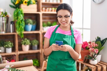 Young hispanic woman florist smiling confident using smartphone at florist