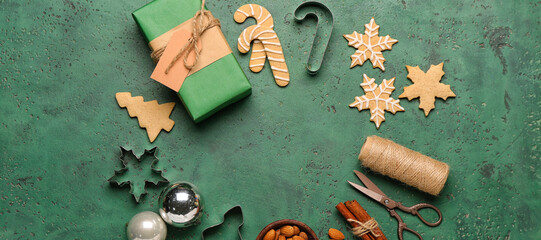 Frame made of tasty Christmas cookies, gift, cutters and decor on green background