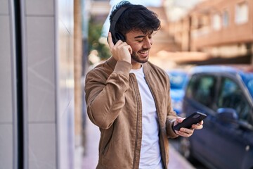 Young hispanic man smiling confident listening to music at street