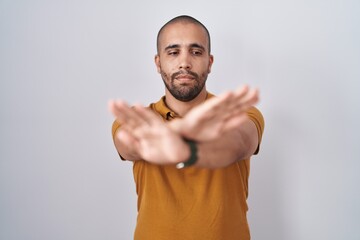 Hispanic man with beard standing over white background rejection expression crossing arms and palms...