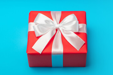 Close up shot of gift box wrapped in red paper and decorated with satin ribbon bow, isolated over bright blue background