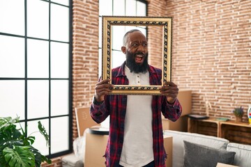 African american man putting face in empty frame angry and mad screaming frustrated and furious, shouting with anger. rage and aggressive concept.
