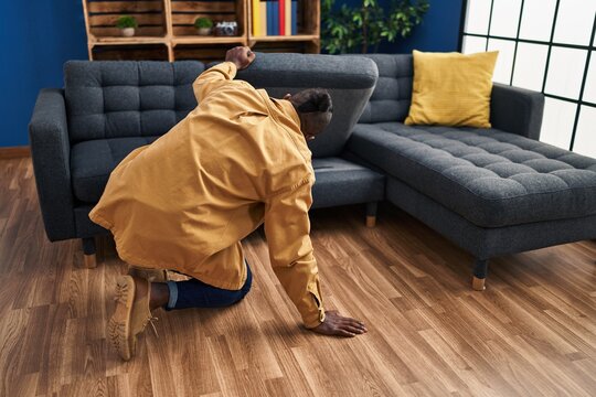 Young african american man looking for something under sofa at home