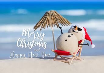 Obraz premium Sandy Christmas Snowman is sunbathing on a sun lounge next to a thatched umbrella, wearing sunnies. Christmas and new year wishes on a background