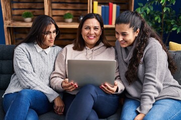 Three woman using laptop sitting on sofa at home