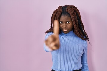 African woman standing over pink background pointing with finger up and angry expression, showing no gesture