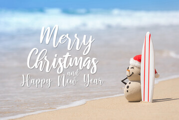 Sandy Christmas Snowman is watching the waves, standing on beautiful beach with a surf board....