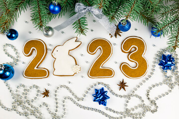 Greeting card 2023. Rabbit and gingerbread numbers. Decor in the form of spruce branches and blue balls.