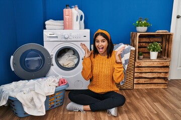 Young hispanic woman doing laundry celebrating mad and crazy for success with arms raised and closed eyes screaming excited. winner concept