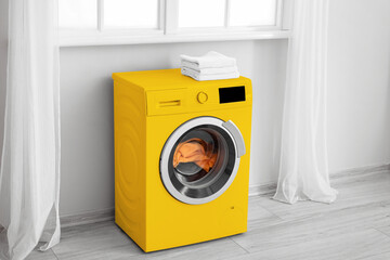 Modern yellow washing machine with laundry near window