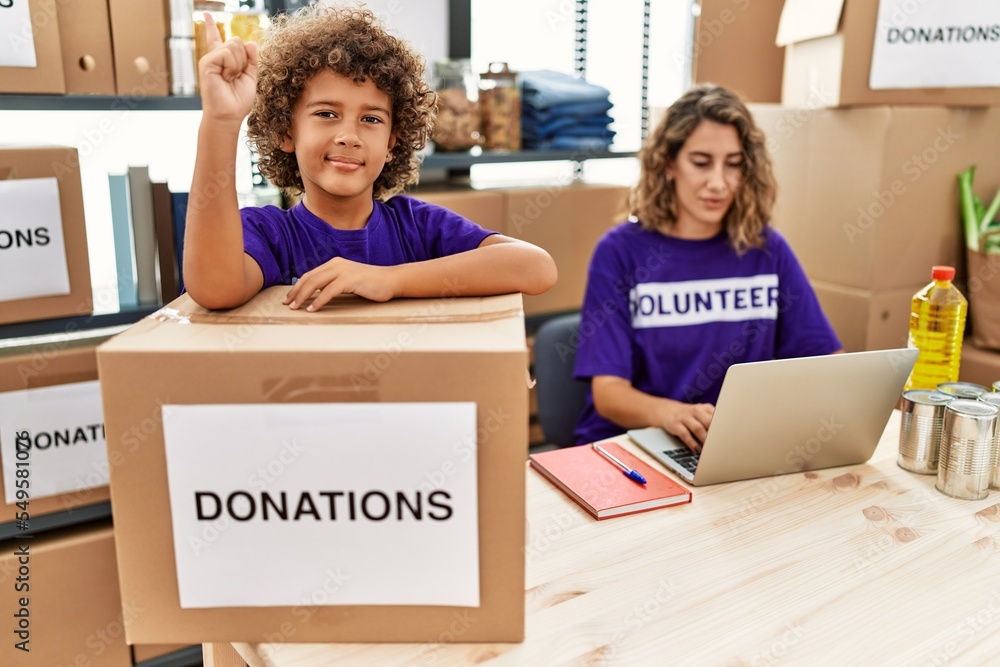 Sticker young mother with little son wearing volunteer t shirt at donations stand smiling with an idea or qu