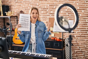 Young caucasian woman doing online music tutorial showing music sheet screaming proud, celebrating...