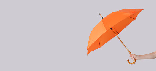 Hand holding stylish orange umbrella on grey background with space for text - Powered by Adobe