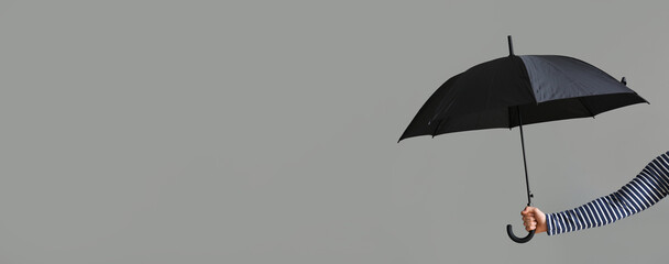 Hand holding stylish black umbrella on grey background with space for text © Pixel-Shot