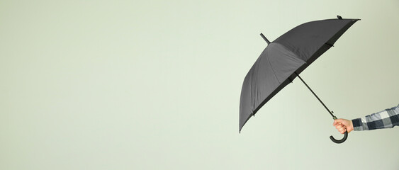 Hand holding stylish black umbrella on light background with space for text