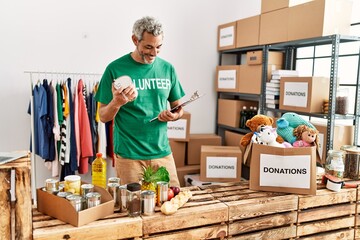Middle age grey-haired man volunteer reading document holding canned food at charity center