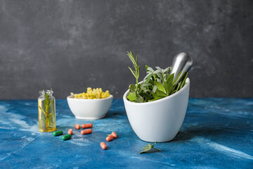 Mortar with herbs, pills and bottle of essential oil on color table
