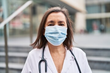 Middle age woman wearing doctor uniform and medical mask standing at street