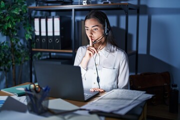 Young brunette woman wearing call center agent headset working late at night asking to be quiet...