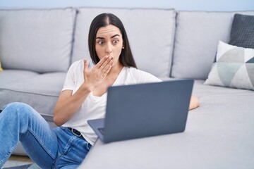Young brunette woman using laptop at home covering mouth with hand, shocked and afraid for mistake....