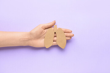 Female hand and paper lungs on lilac background