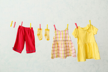 Different baby clothes hanging on rope against light background