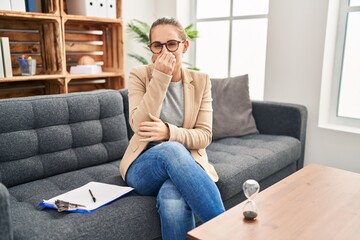 Fototapeta premium Young woman working at consultation office smelling something stinky and disgusting, intolerable smell, holding breath with fingers on nose. bad smell