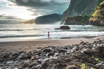 Woman walking on beautiful beach and enjoying the atmospheric morning atmosphere. Seixal beach, Madeira Island, Portugal, Europe.