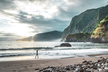 Woman walking on beautiful beach and enjoying the atmospheric morning atmosphere. Seixal beach, Madeira Island, Portugal, Europe.