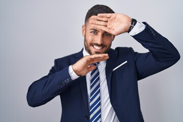Handsome hispanic man wearing suit and tie smiling cheerful playing peek a boo with hands showing face. surprised and exited