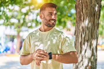 Young hispanic man smiling confident looking watch at park