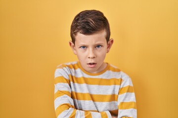 Young caucasian kid standing over yellow background skeptic and nervous, disapproving expression on face with crossed arms. negative person.