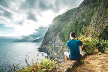Naklejka premium Sporty man looking at waterfall flowing into the sea in atmospheric morning atmosphere. Viewpoint Véu da Noiva, Madeira Island, Portugal, Europe.
