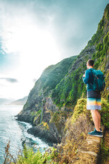 Naklejka premium Sporty man looking at waterfall flowing into the sea in atmospheric morning atmosphere. Viewpoint Véu da Noiva, Madeira Island, Portugal, Europe.