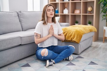 Fototapeta premium Young woman doing yoga exercise sitting on floor at home
