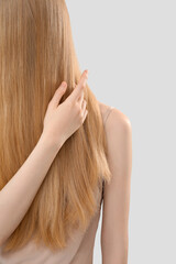 Fototapeta premium Blonde woman touching long hair on light background, closeup