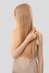 Blonde woman touching long hair on light background